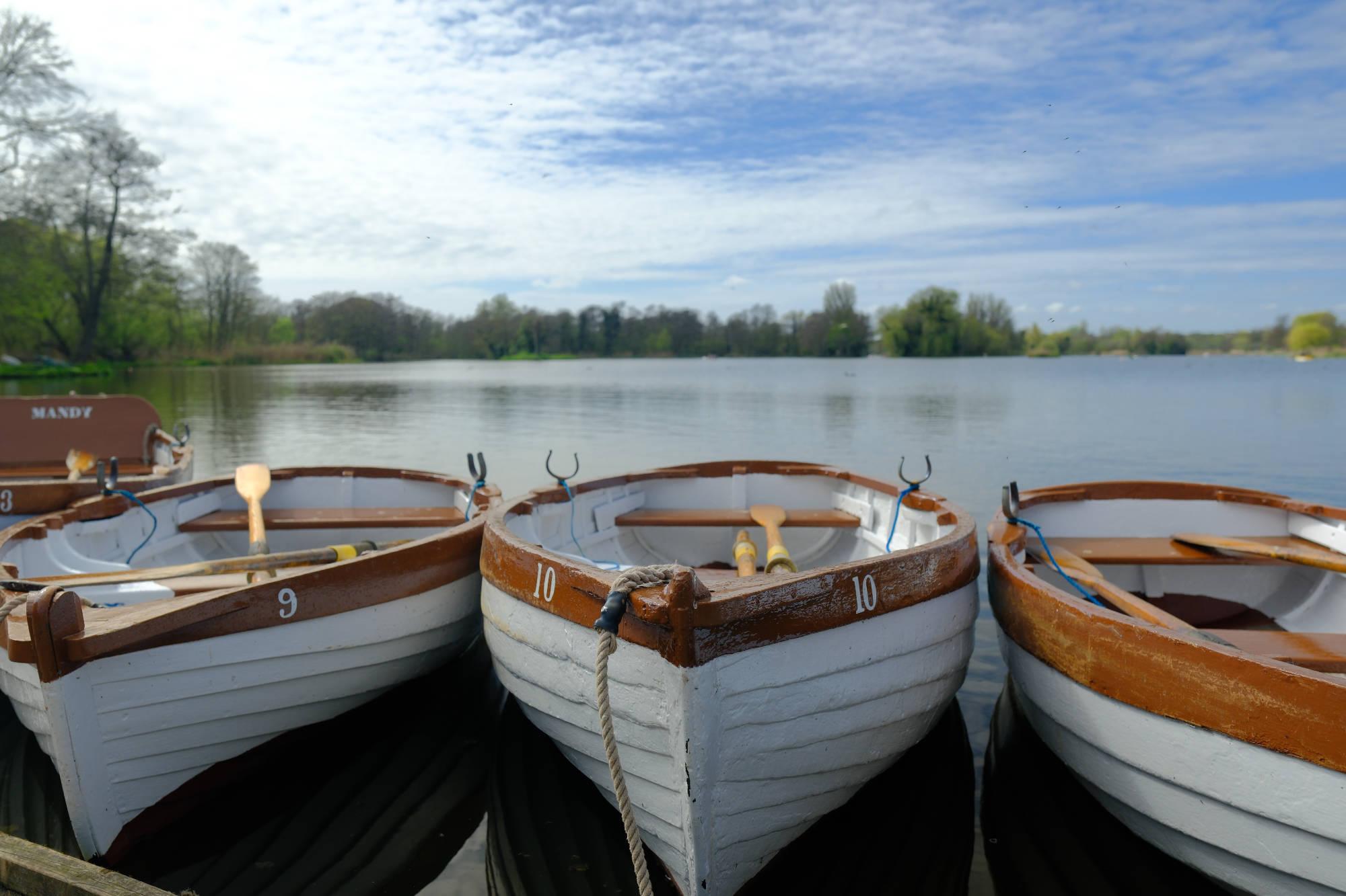 three small boats tied to a dock on a lake with tress and a cloudy, blue sky in the background