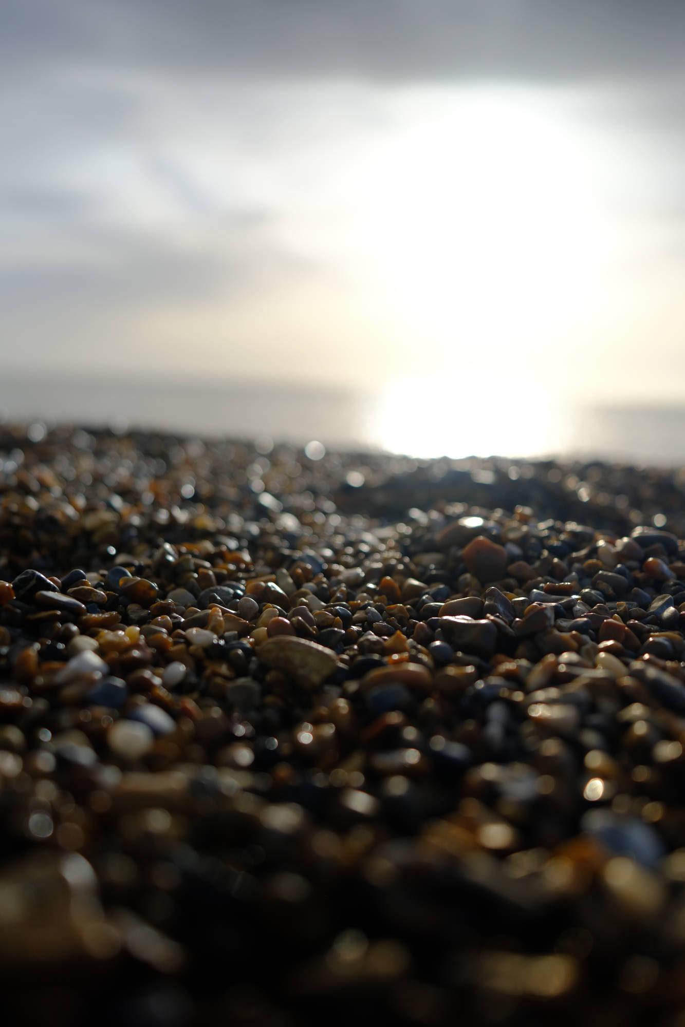 close-up, in-focus shot of a beach filled with pebbles and the bright sky in the background