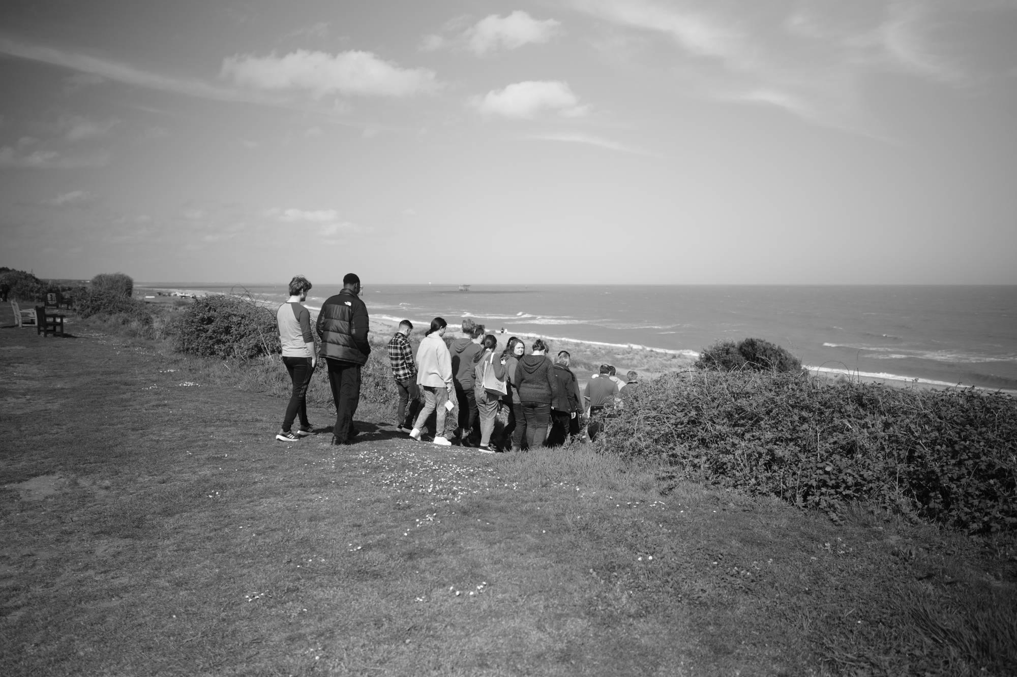 group of people walking down a slope to a beach shoreline, grayscale