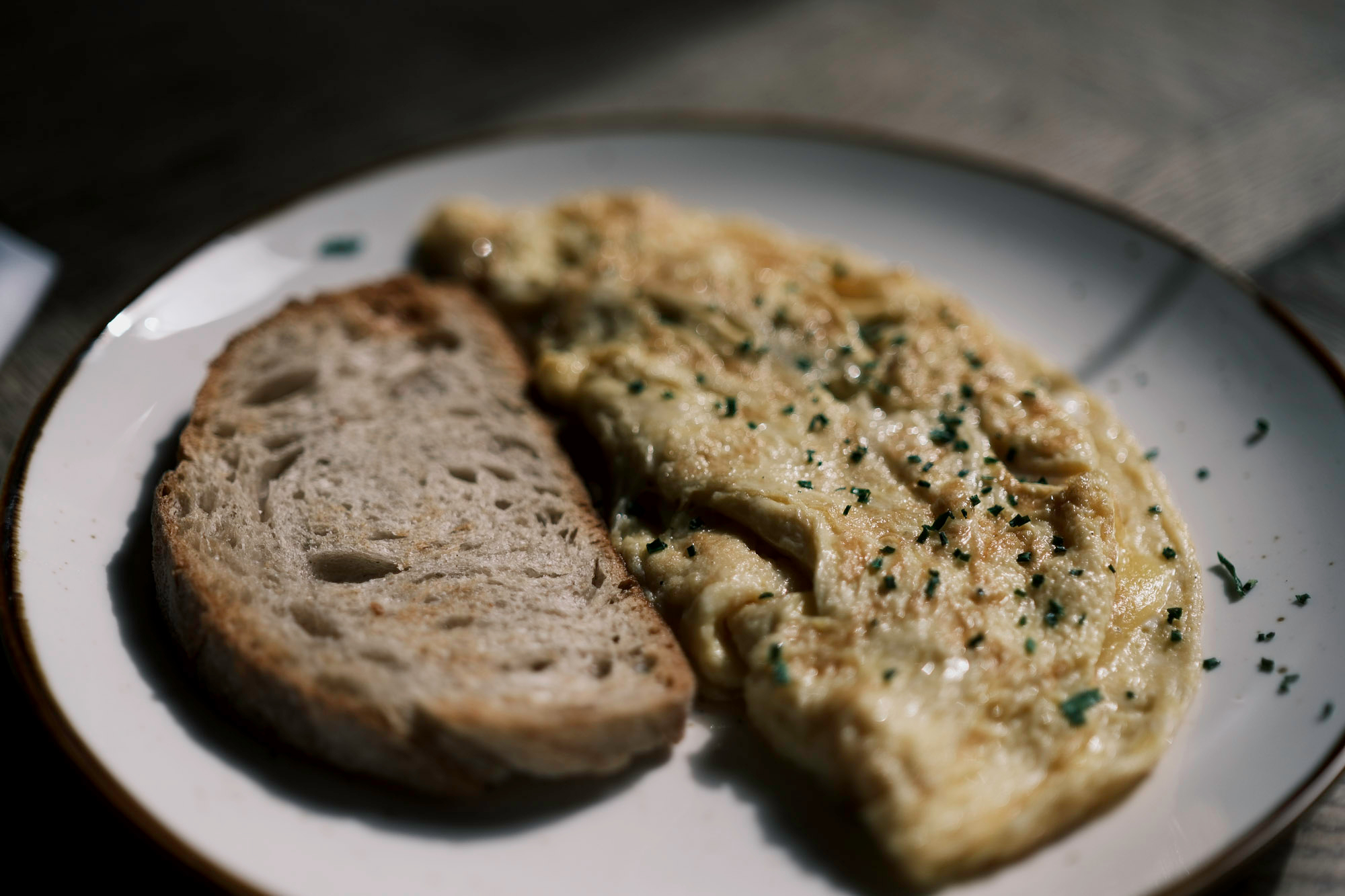 folded ham and cheese omelette with the ham concealed and some green herbs sprinkled on top, next to a slice of toasted sourdough bread served on a white plate