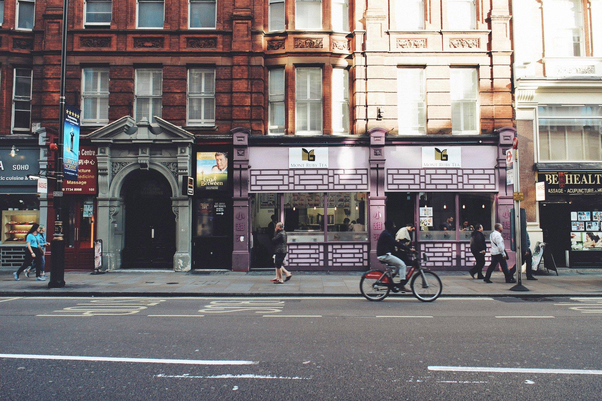 street in Soho, London in the early evening with few people walking on the pavement and one man cycling