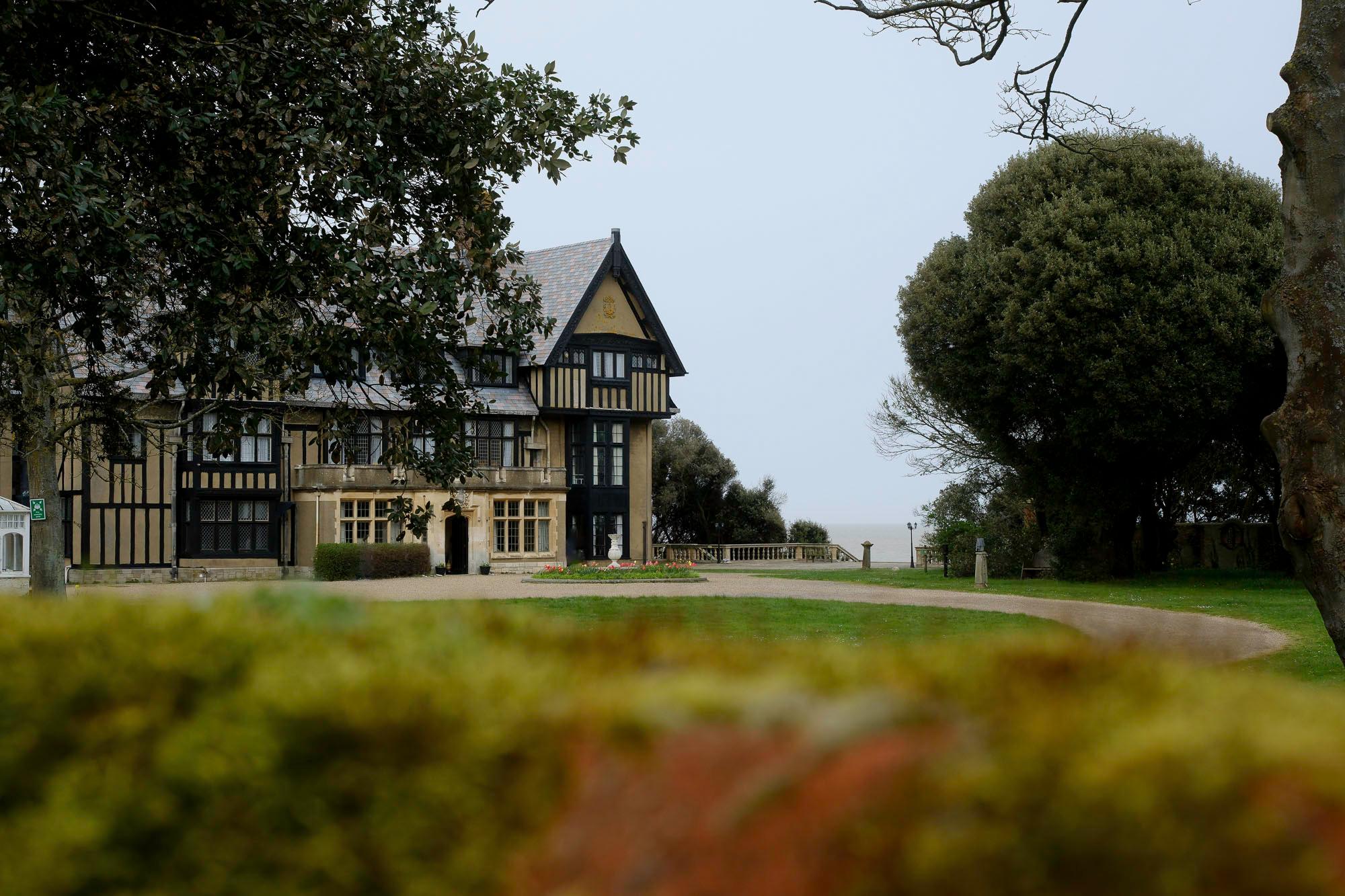 a large manor house sitting on top of a drive, surrounded by well-kept grass and a massive tree